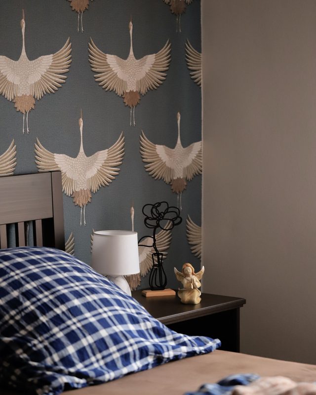 Bedroom with a slate-blue wall of cream and gold crane-motif wallpaper