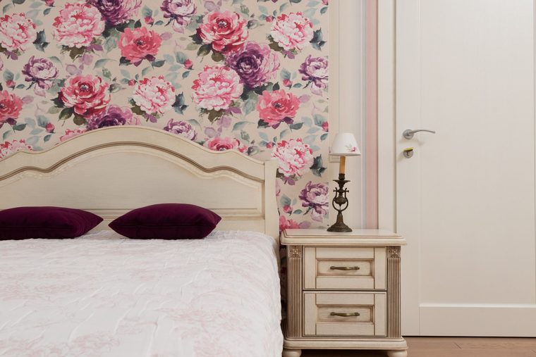 Bedroom with soft watercolour floral wallpaper behind a carved headboard